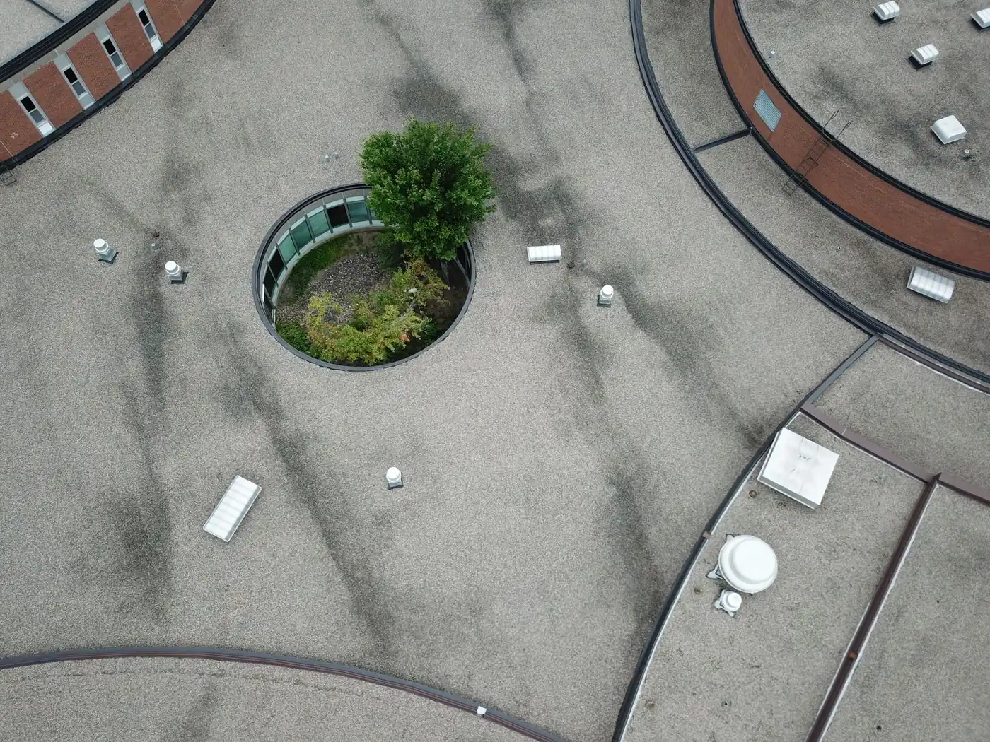 Aerial view of a gravel-surfaced built-up flat roof with vents, skylights, and a round courtyard opening