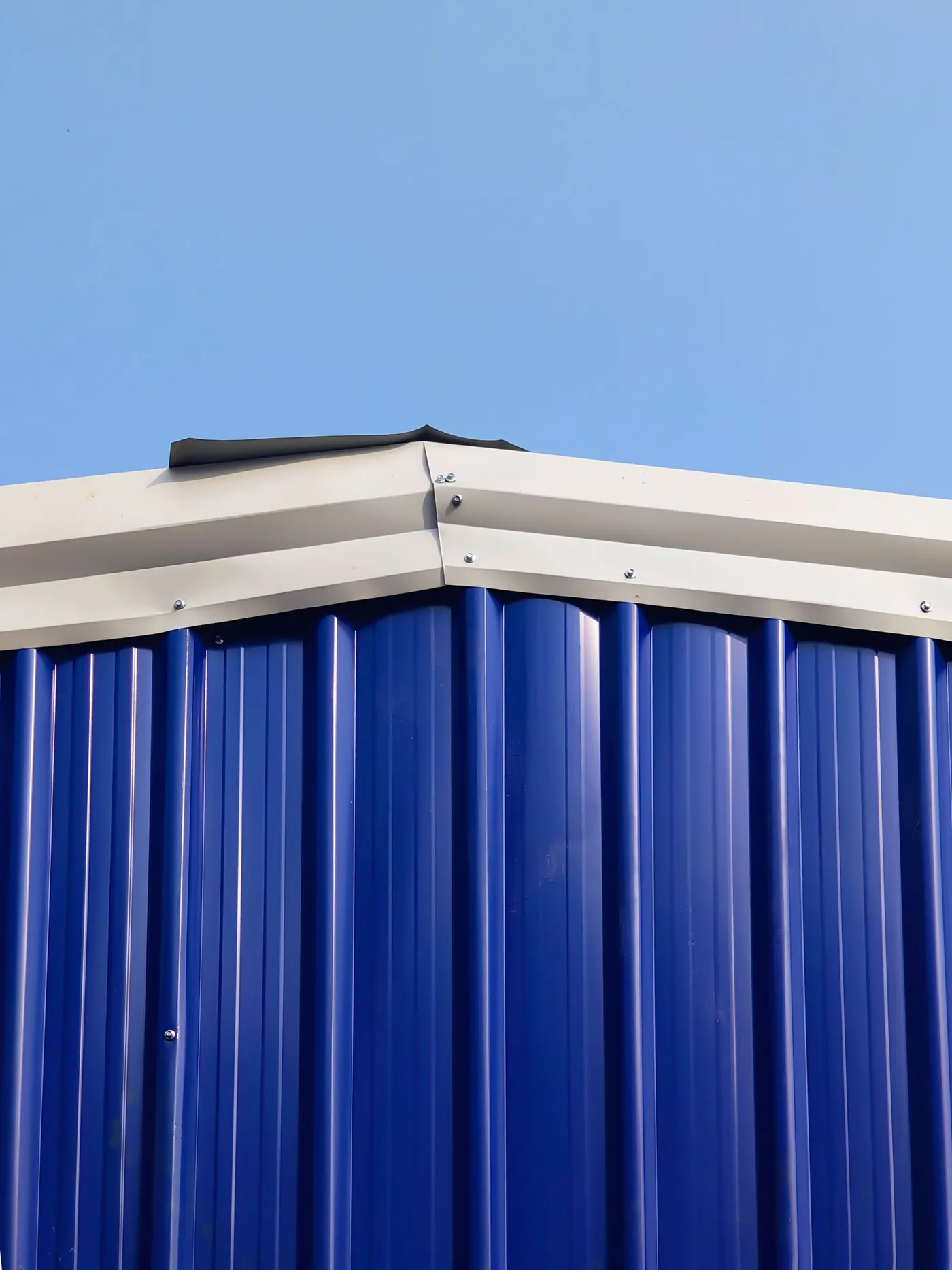 Blue corrugated metal panels and ridge trim on a metal building under a clear sky