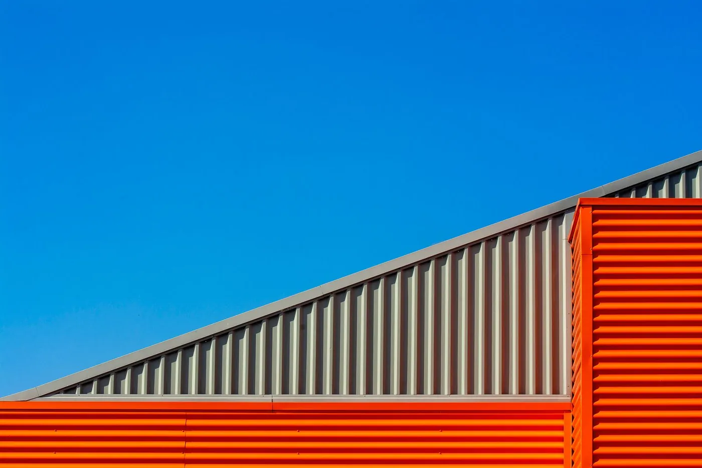 Gray ribbed metal gable cladding above the orange corrugated wall of an industrial building