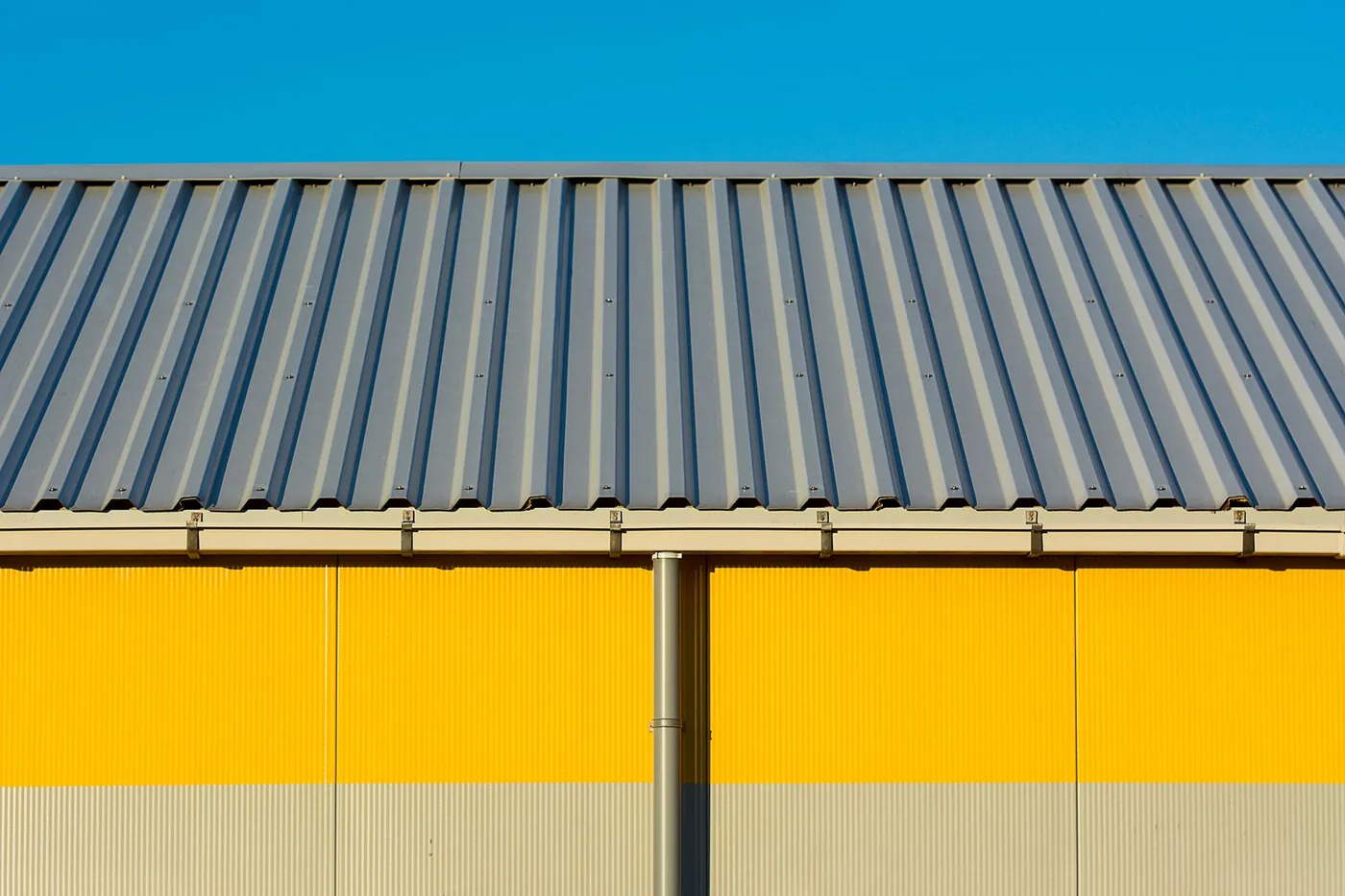 Gray corrugated metal roof with gutter and downspout on a yellow industrial building